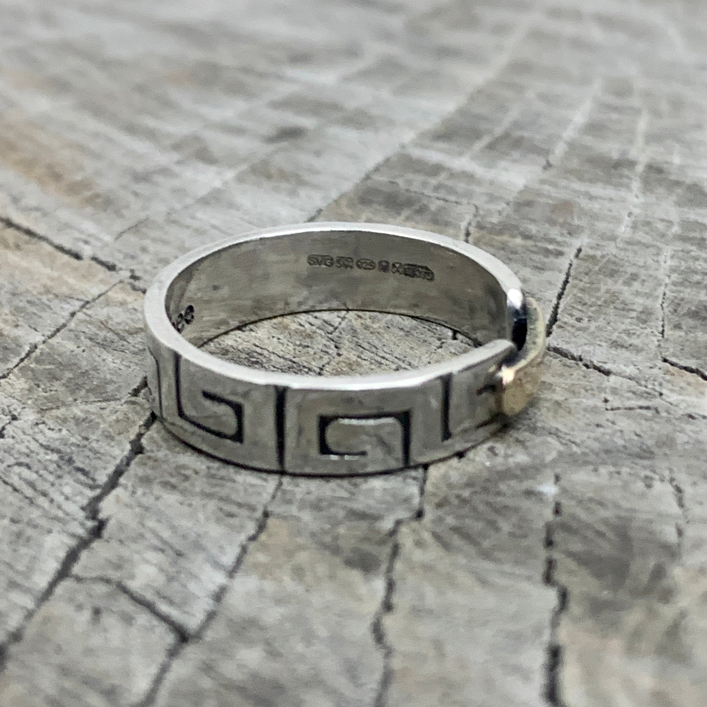 a hallmarked solid silver greek style ring with a gold bar on a wooden background
