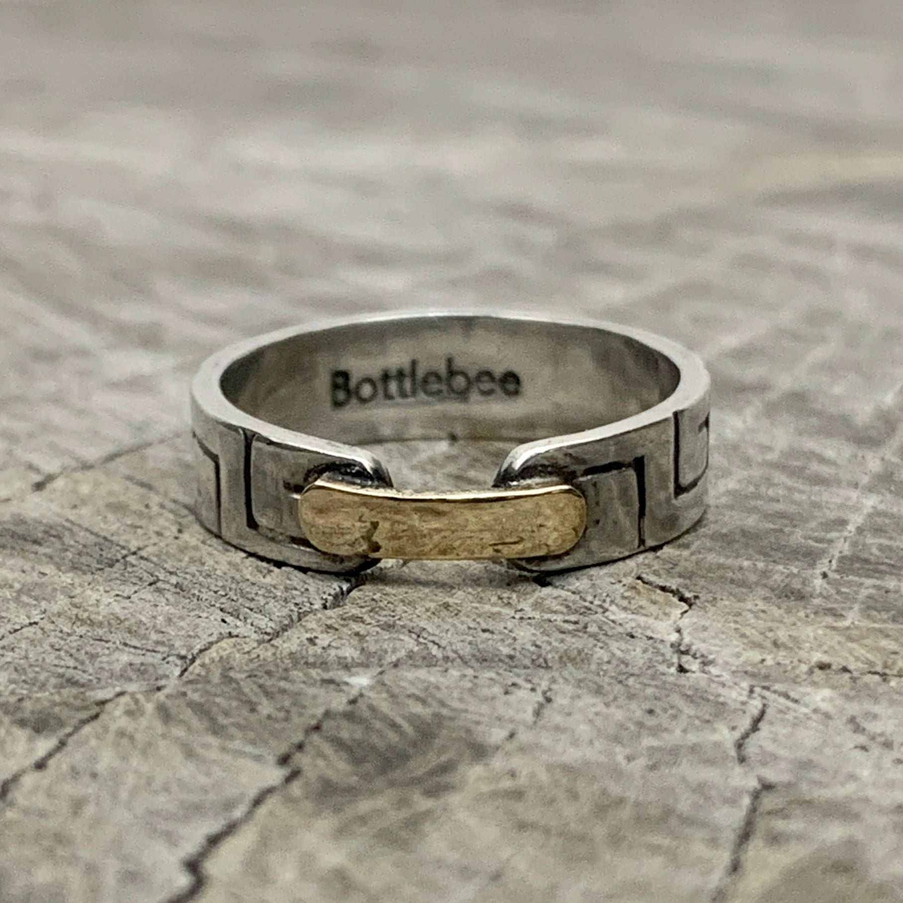 a silver and gold ring with Bottlebee stamped inside. The ring has a greek style pattern