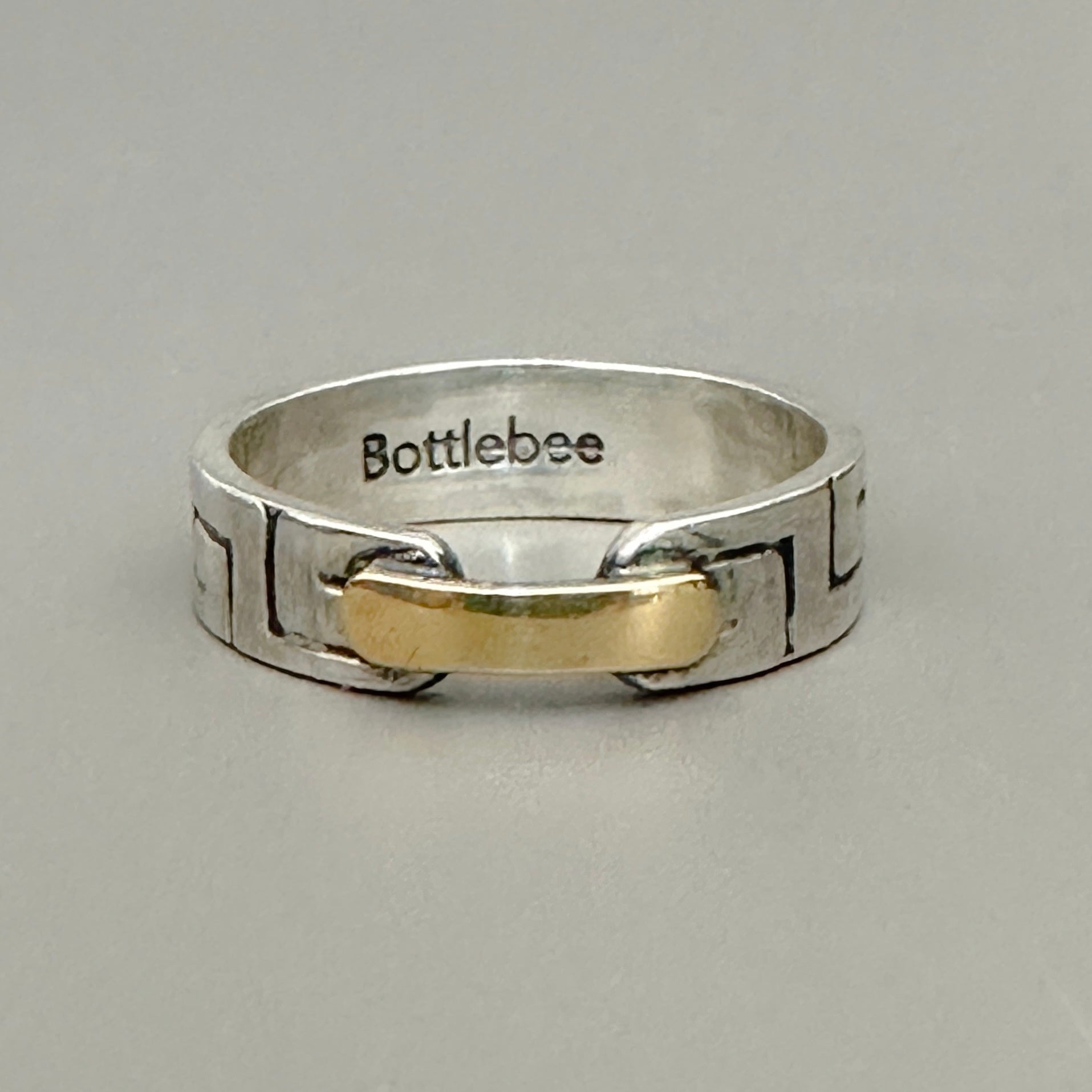 a silver and gold ring with Bottlebee stamped inside. The ring has a greek style pattern