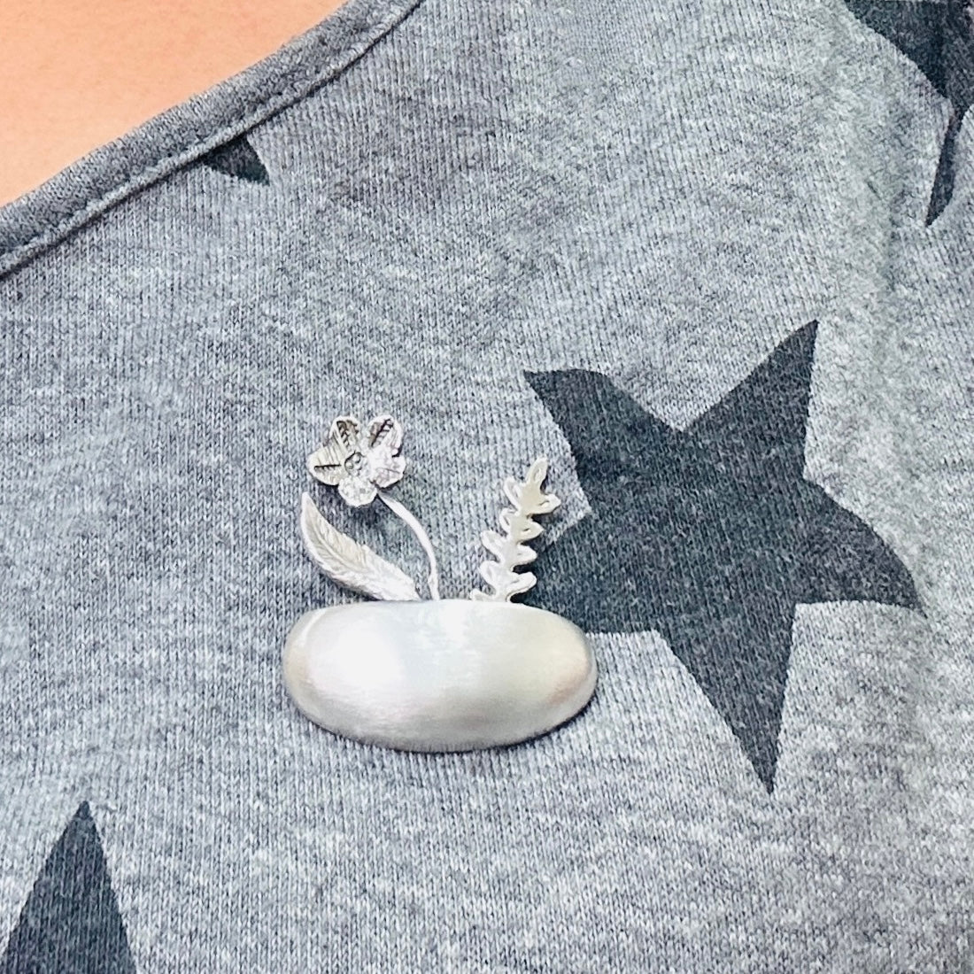 Silver brooch with floral design on a grey shirt with star pattern handmade in nottingham by bottlebee