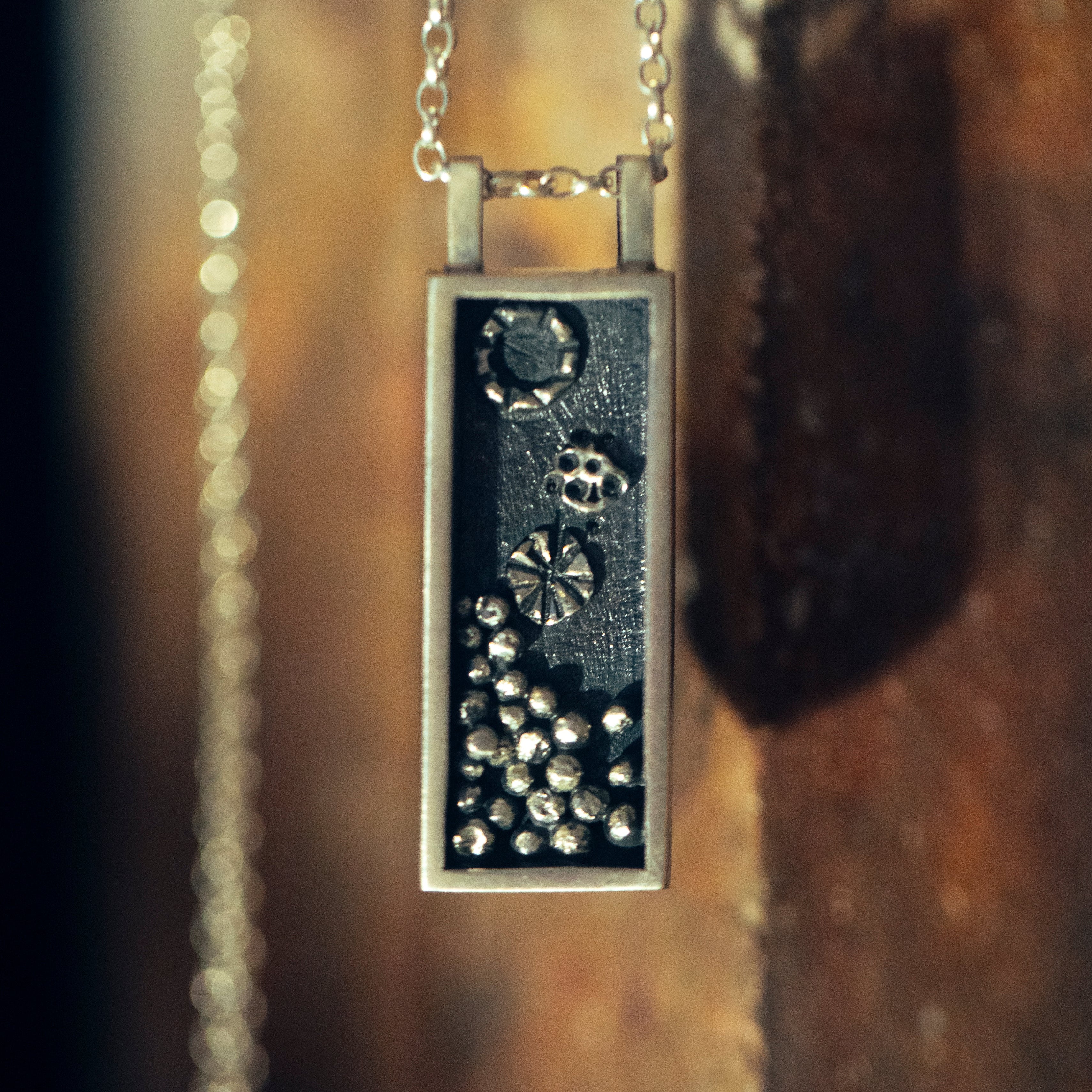 Silver oxidised pendant necklace with intricate details and accents on a textured surface