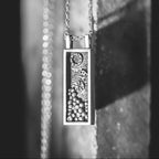 Close-up of a silver necklace with a rectangular pendant on a dark background
