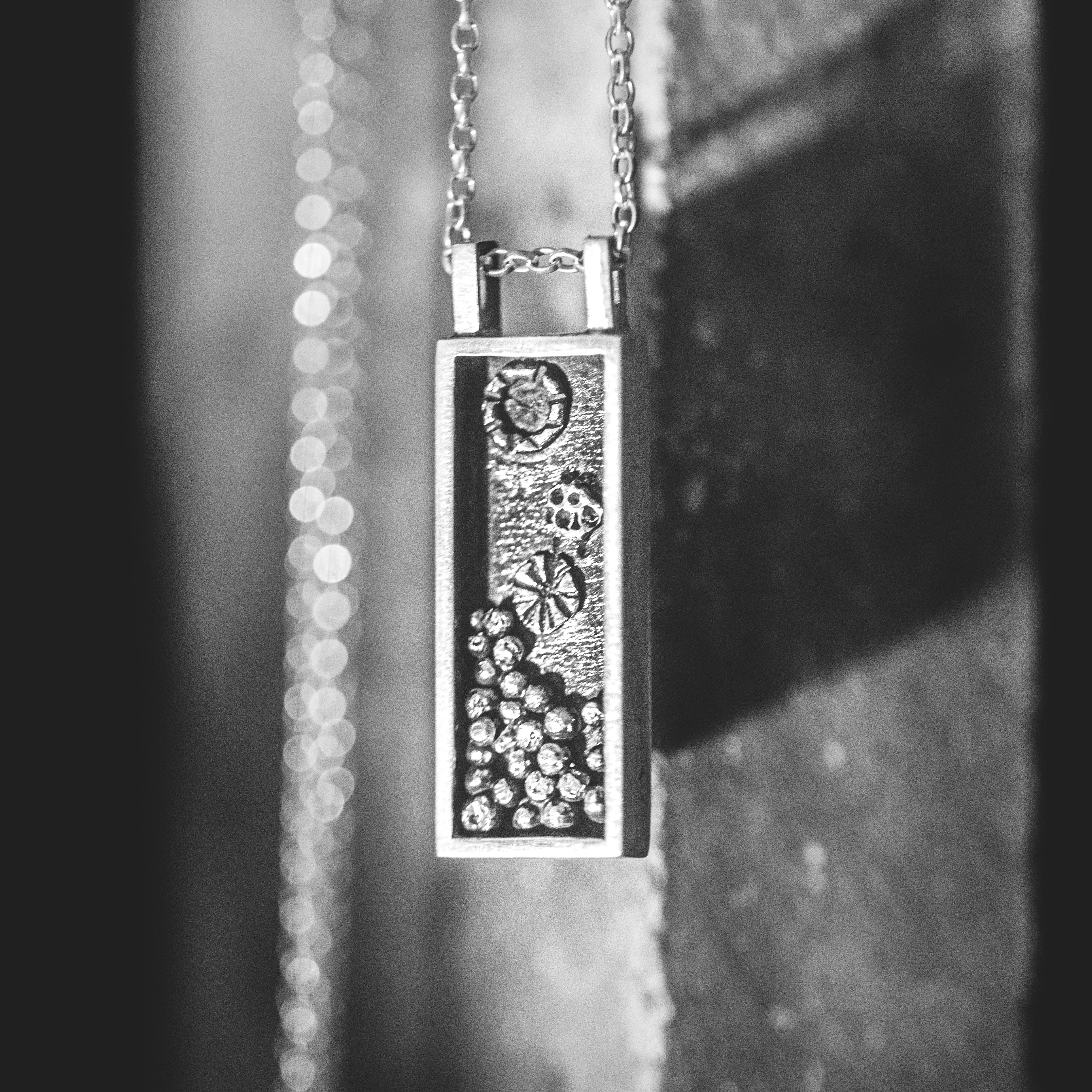 Close-up of a silver necklace with a rectangular pendant on a dark background