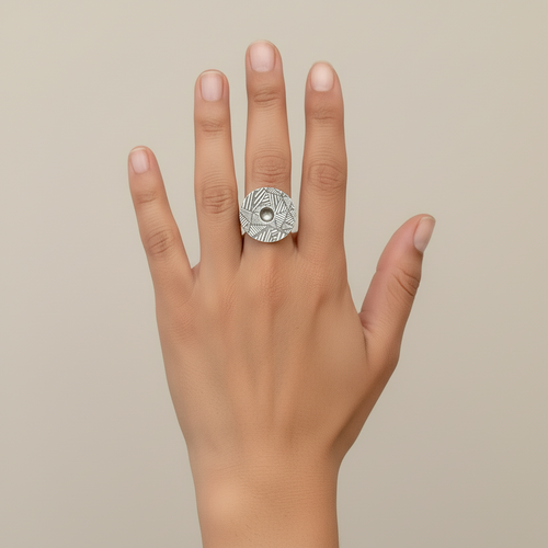 Silver ring with geometric pattern with a moving ball being held with a finger against a neutral background