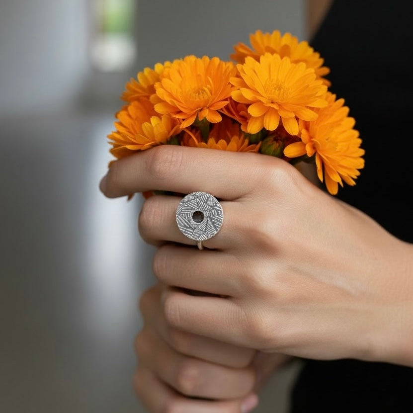 Woman’s hand holding a bouquet of orange flowers with a decorative statement sterling silver handmade geometric patterned and oxidised kinetic ring made in Nottingham by a small one woman business called Bottlebee