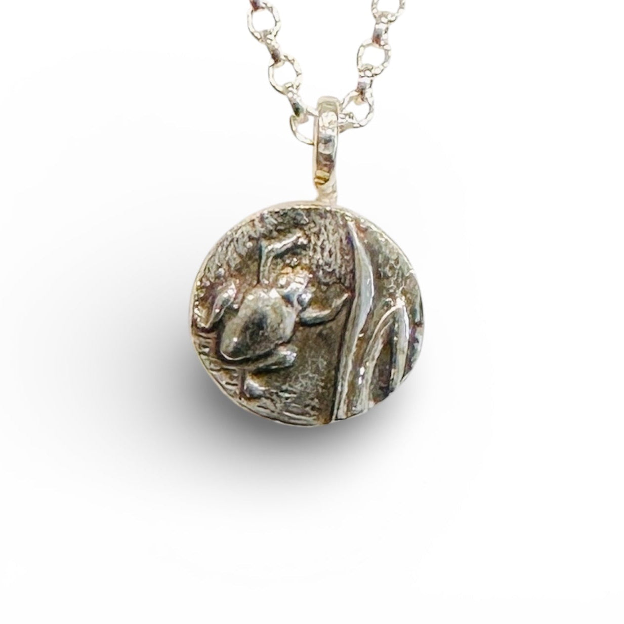 Silver necklace with a round pendant with a raised oxidised frog on a white background handmade by bottlebee in nottingham who makes sustainable jewellery