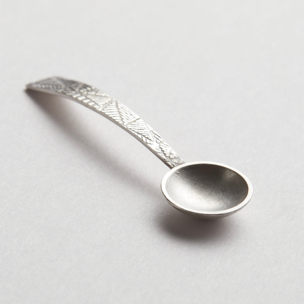 Silver decorative spoon on a light grey background. sterling silver christening baptism spoon for godson goddaughter with engraved design on a textured stone surface being held in a hand nottingham