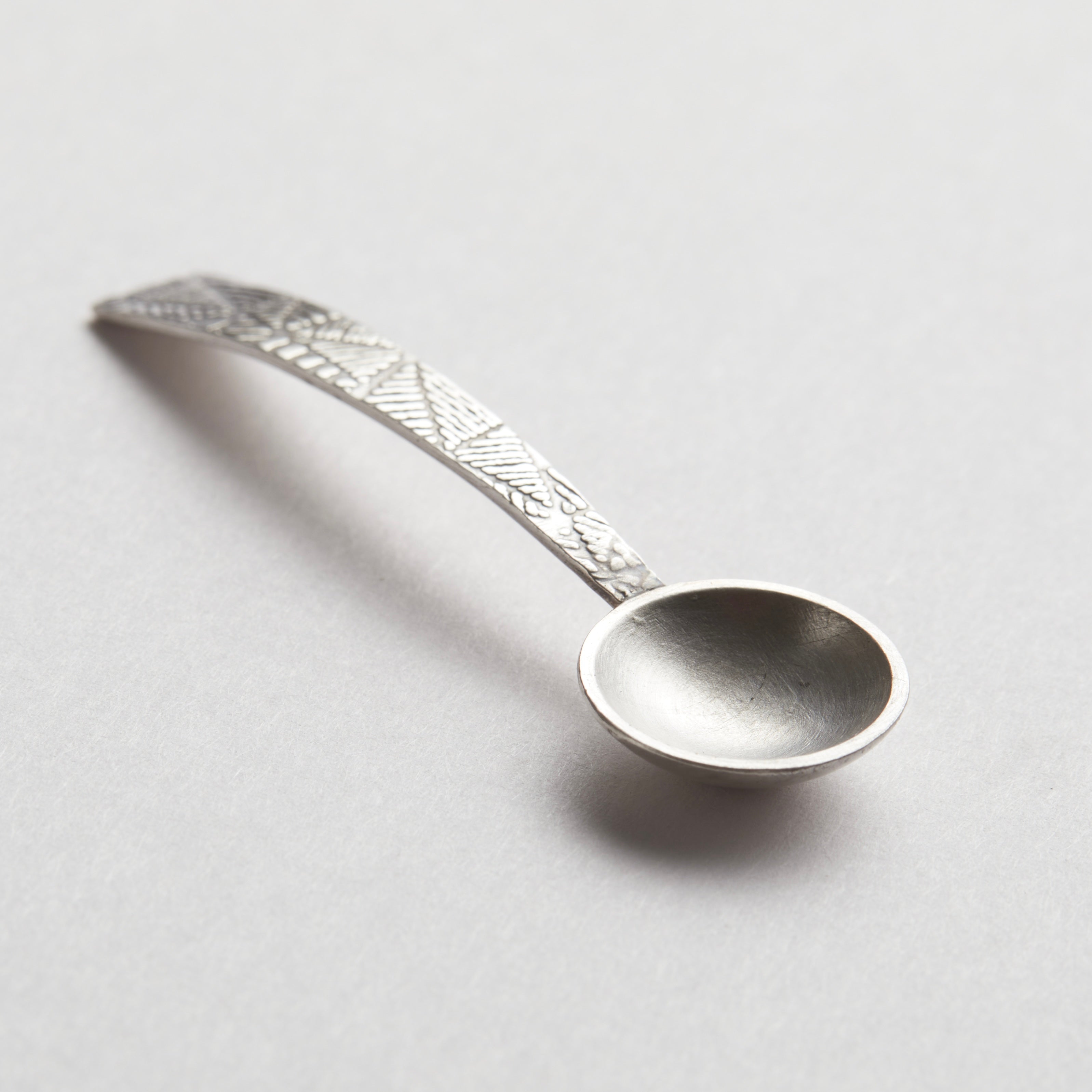 Silver decorative spoon on a light grey background. sterling silver christening baptism spoon for godson goddaughter with engraved design on a textured stone surface being held in a hand nottingham