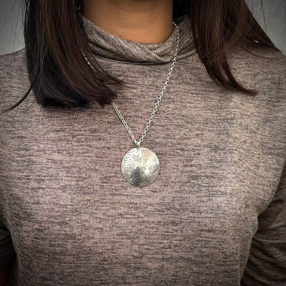 Woman wearing a silver hummingbird necklace with a round pendant handmade by bottlebee in nottingham