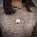 Woman wearing a silver hummingbird necklace with a round pendant handmade by bottlebee in nottingham