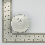Silver circular jewellery impression die with a mother goddess design on a ruler for scale
