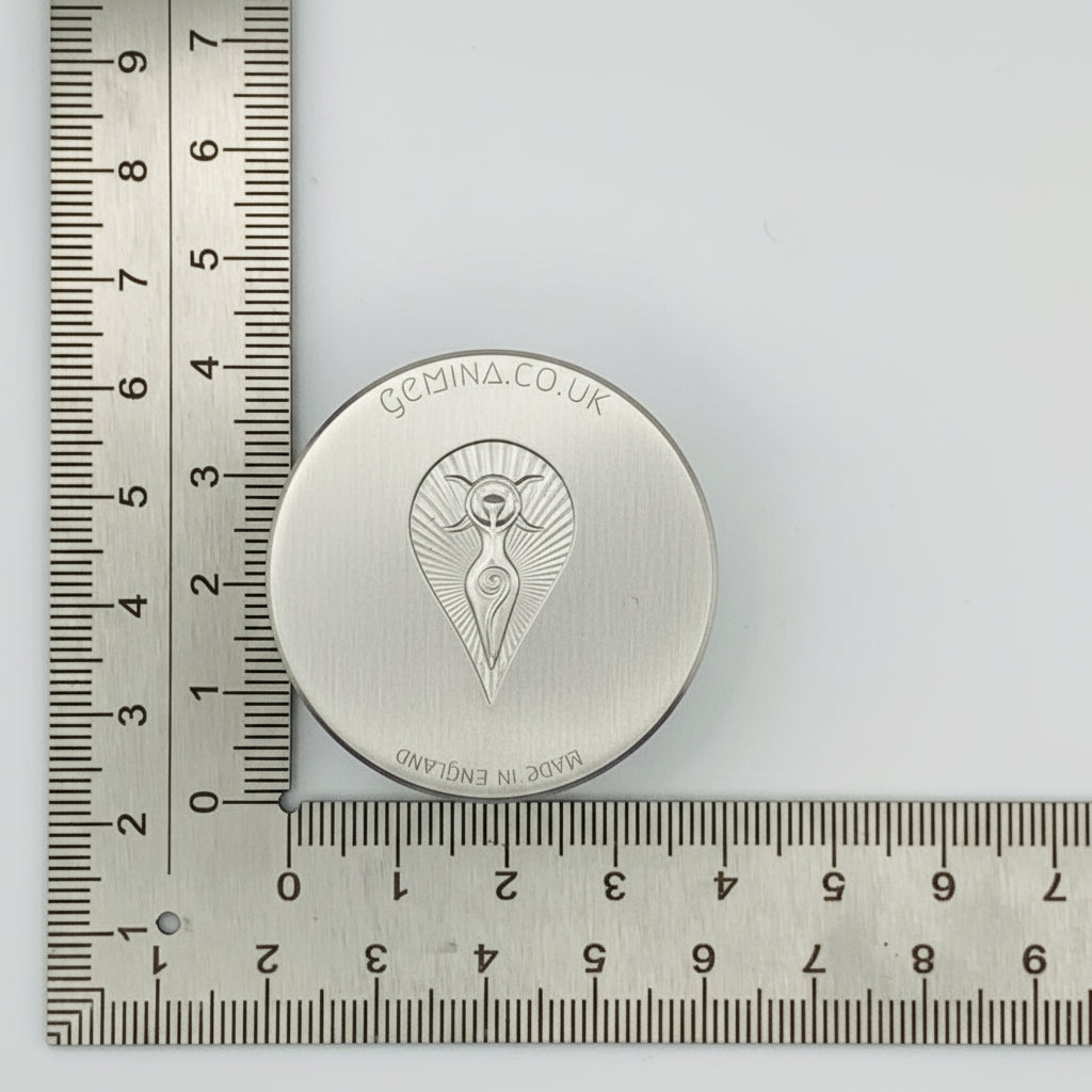 Silver circular jewellery impression die with a mother goddess design on a ruler for scale