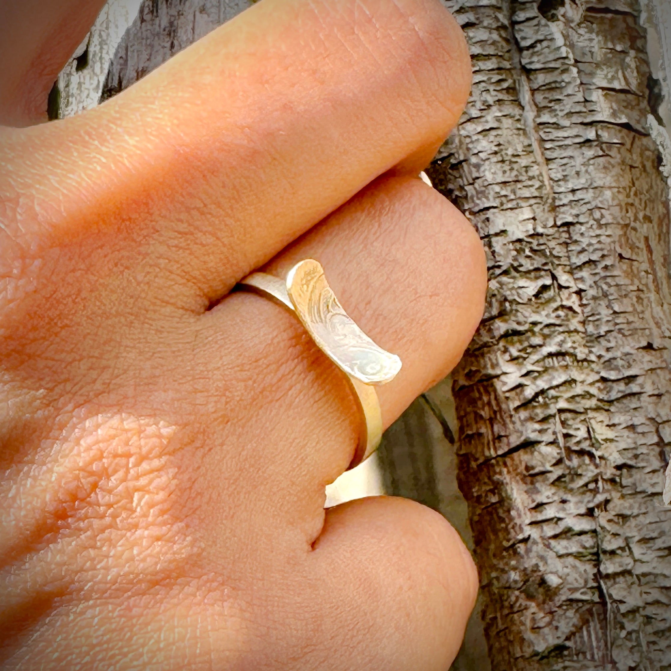 Solid 9ct yellow gold ring on a finger with a tree trunk background