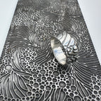 Silver wedding ring on a textured metal pattern plate used to make the wedding ring, which is handmade by Bottlebee who makes sustainable bespoke jewellery in Nottingham
