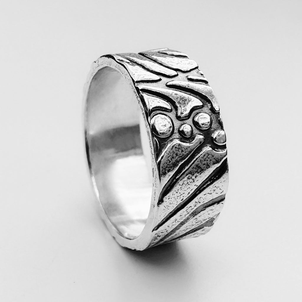 Solid silver unique wedding ring with intricate design on a light background Silver unique wedding ring with intricate design on a textured metal surface handmade by Bottlebee who makes sustainable bespoke jewellery in Nottingham