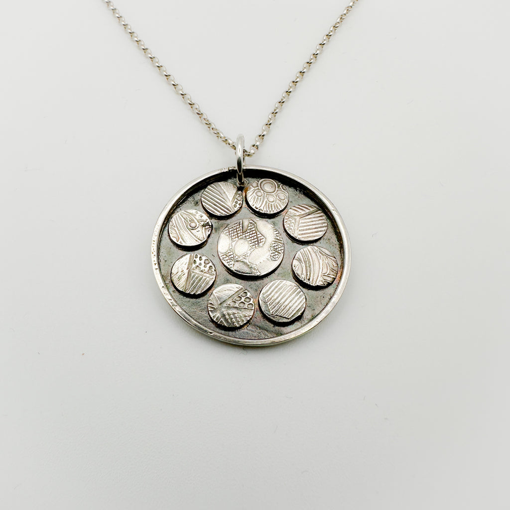 Silver necklace with a round pendant featuring raised designs on silver oxidised discs handmade by Bottlebee in Nottingham