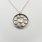 Silver necklace with a round pendant featuring raised designs on silver oxidised discs handmade by Bottlebee in Nottingham