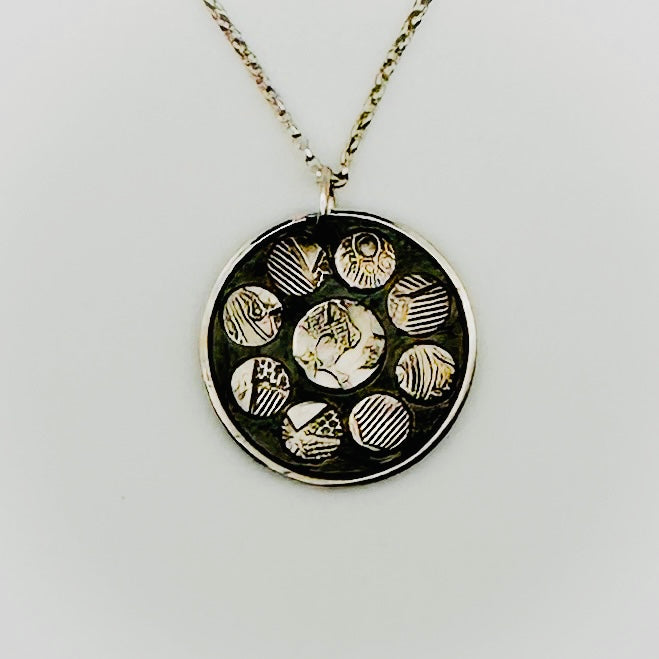 Necklace with a round pendant featuring embossed designs on circular raised discs a light grey background