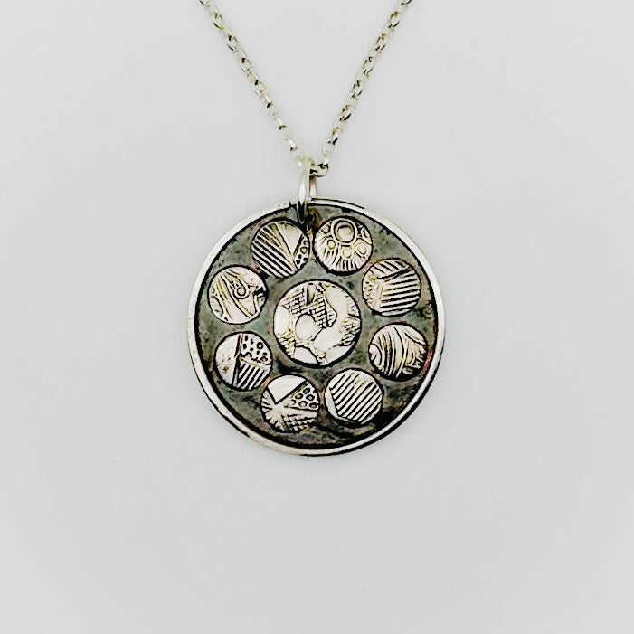 Sterling silver necklace with a round pendant featuring embossed designs on raised patterned discs, bespoke silver and gold jewellery made in Nottingham