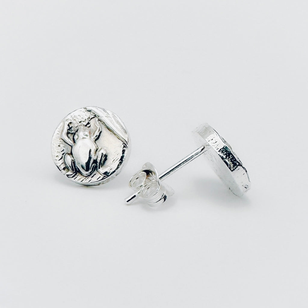 Silver round earrings with a frog impression on a light grey background