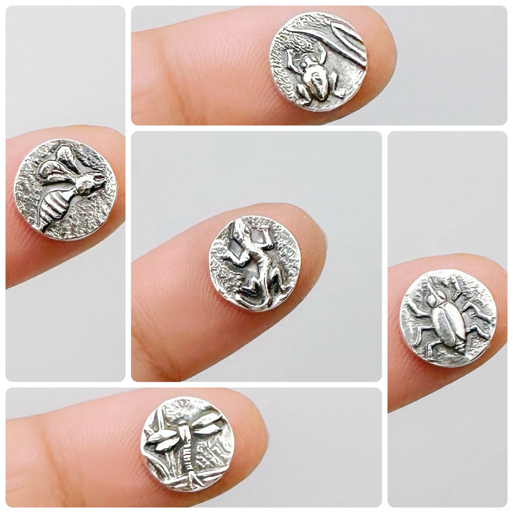 Silver insect-themed patterns called Pond Life held on fingers on a light grey background.  Bottlebee in Nottingham can make any pieces of jewellery with these 5 impressions.