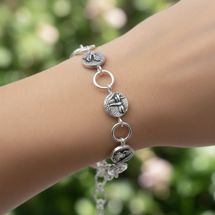 Silver bracelet with insect charms on a wrist against a green nature background Bottlebee in Nottingham handmade jewellery