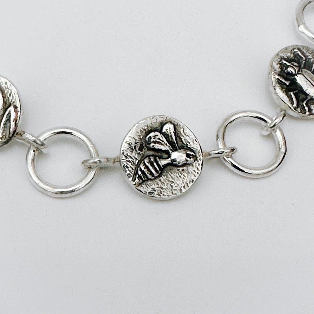 Close-up of a silver bracelet with bee charm on a light grey background made in Nottingham by Bottlebee who mades jewellery that is sustainable