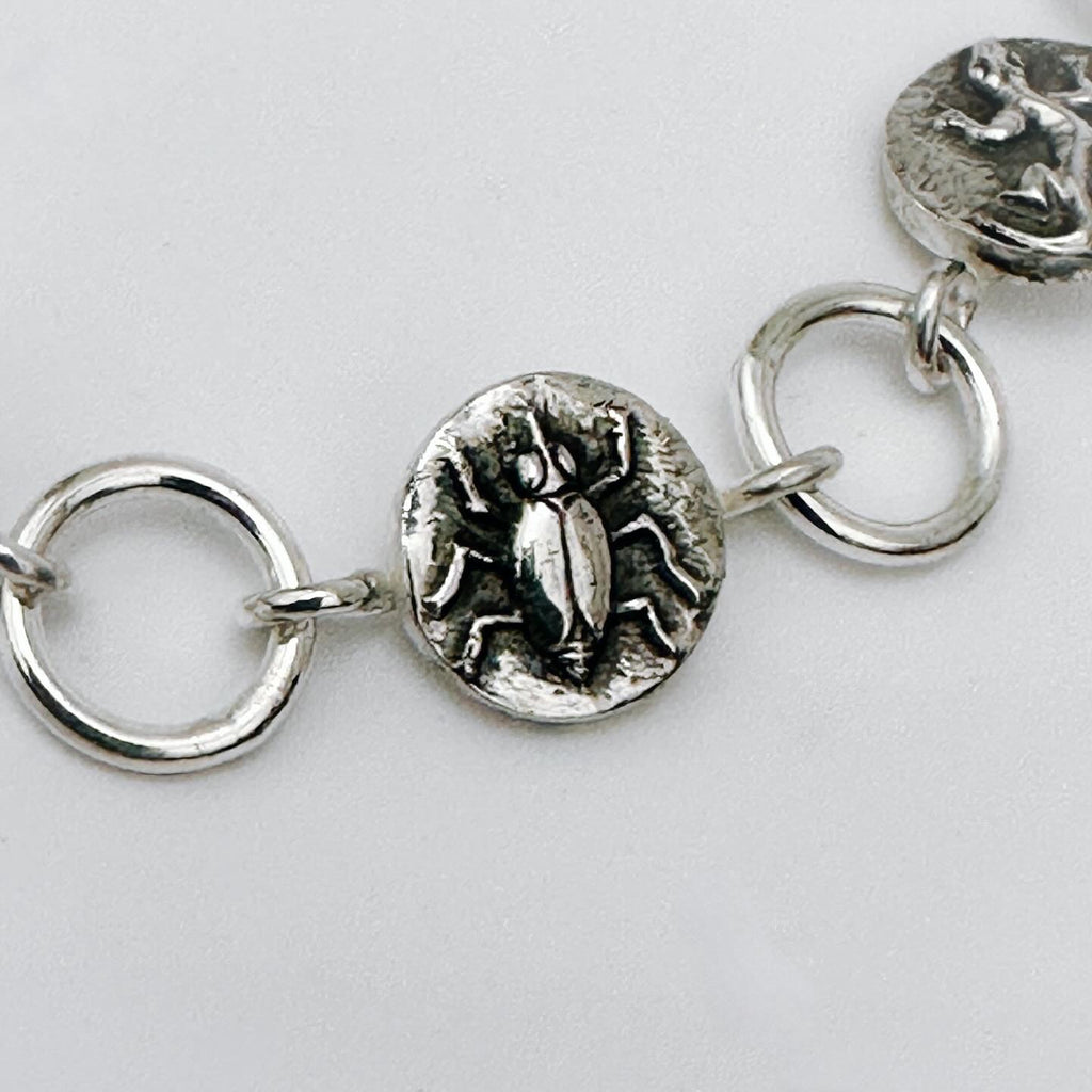 Close-up of a silver bracelet with beetle charm on a light grey background made in Nottingham by Bottlebee who mades jewellery that is sustainable