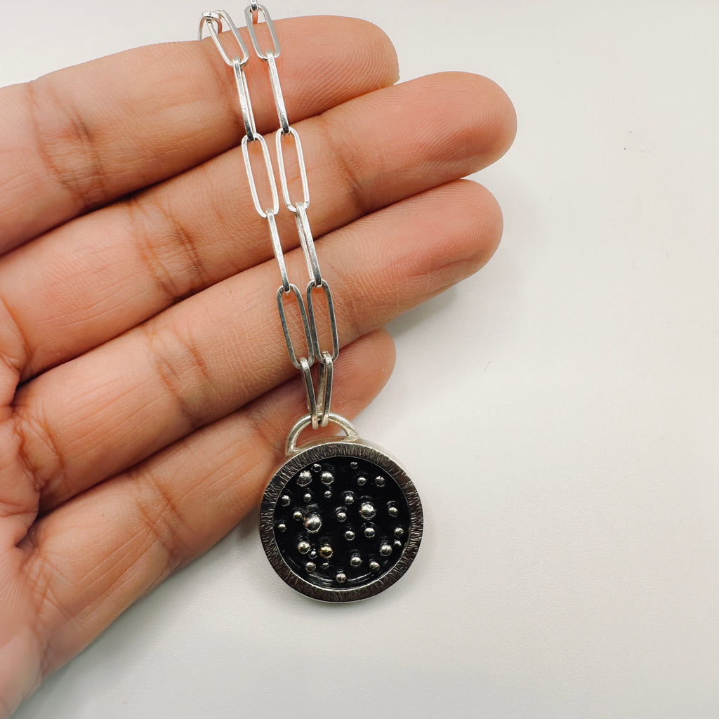 Silver chain with a black and silver and gold pendant with a paperclip chain held in a hand made by hand by Bottlebee in Nottingham 