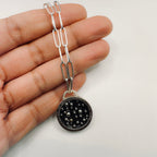 Silver chain with a black and silver and gold pendant with a paperclip chain held in a hand made by hand by Bottlebee in Nottingham 