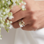 Hand holding a bouquet of white flowers wearing an alternative engagement ring and wedding ring in gold and silver handmade by Bottlebee in Nottingham