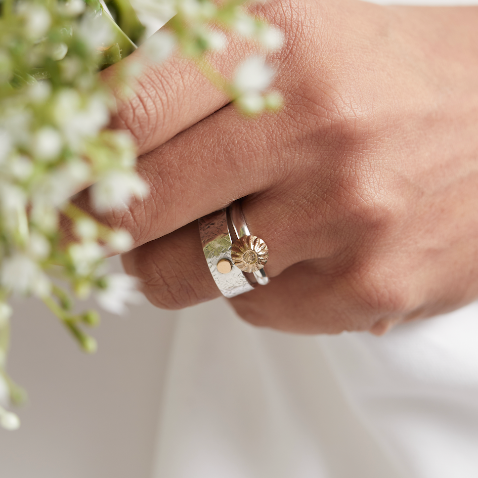 Hand holding a bouquet of white flowers wearing an alternative engagement ring and wedding ring in gold and silver handmade by Bottlebee in Nottingham