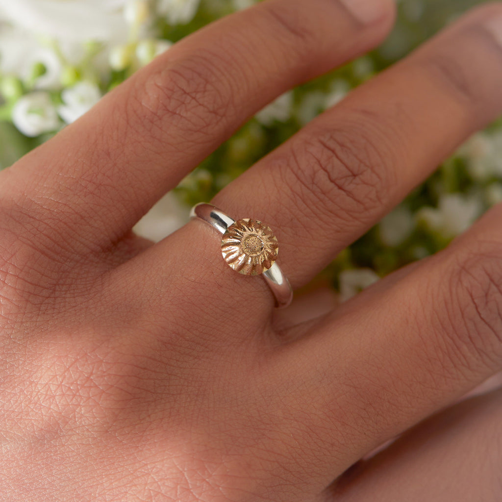 Hand wearing a silver and gold sunflower ring with a blurred floral background