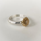 Silver ring with a gold shell-shaped accent on a light grey background