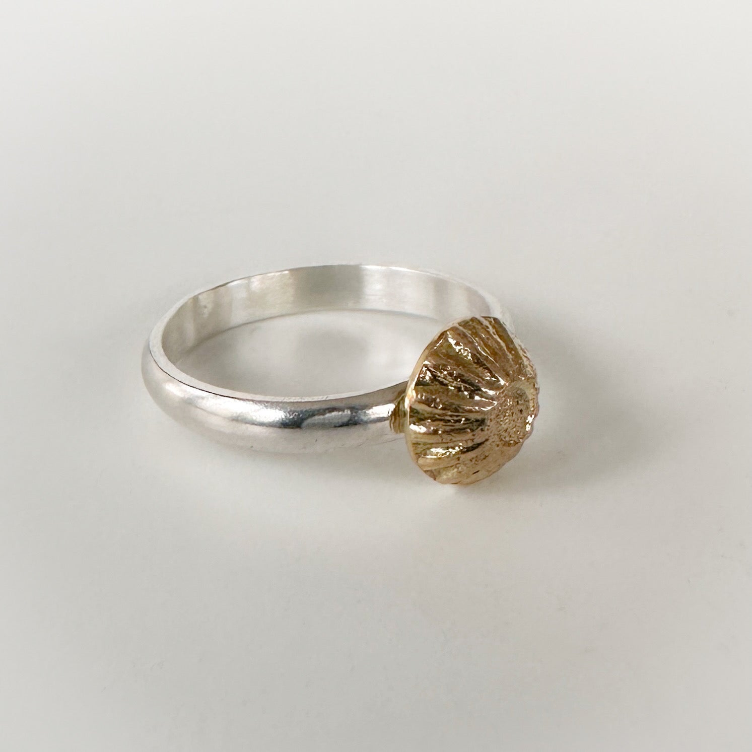 Silver ring with a gold shell-shaped accent on a light grey background
