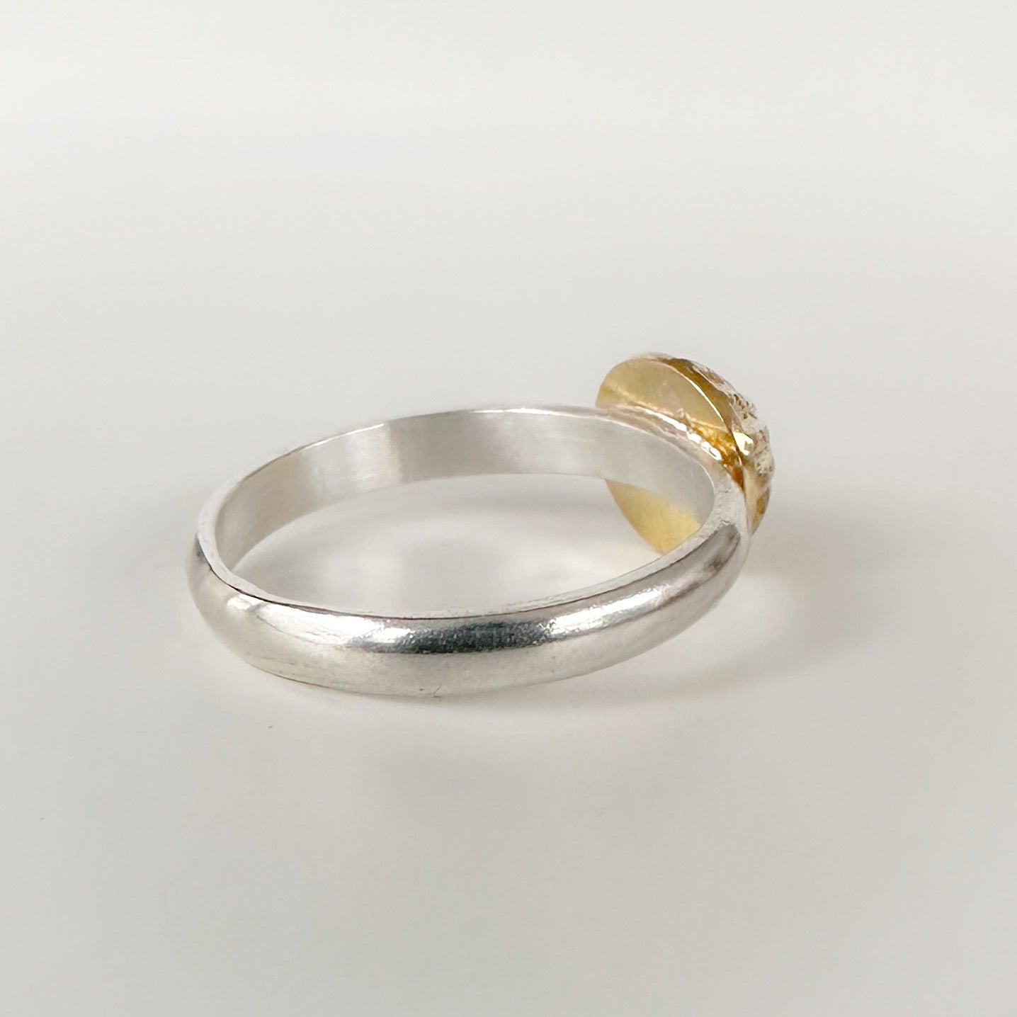 Back view of silver ring with a gold accent alternative engagement ring on a light grey background