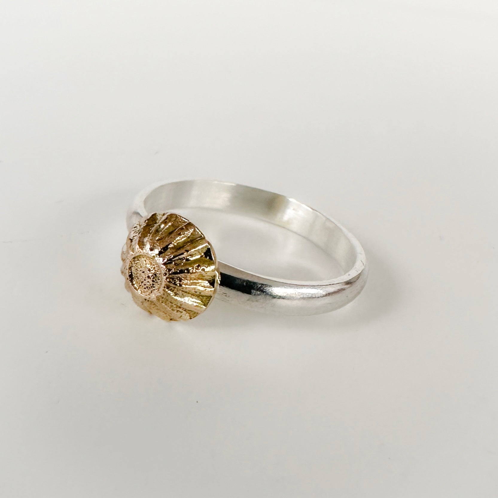 Side view of an alternative engagemnet silver ring with a ribbed textured gold accent on a light grey background