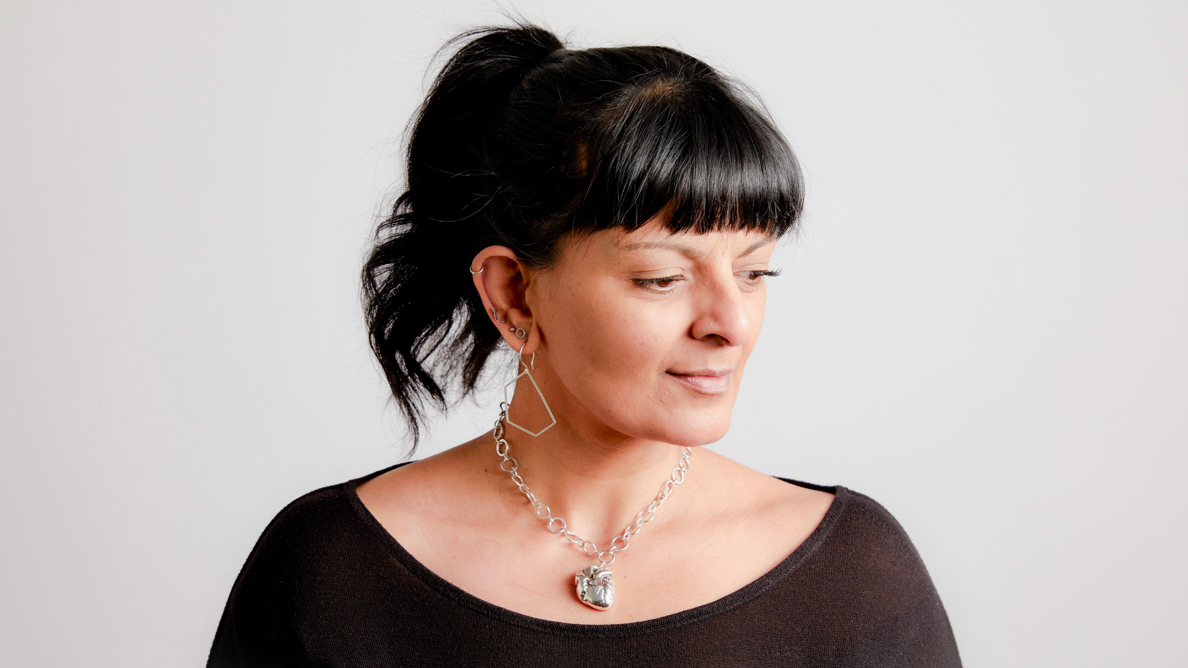 Woman wearing a necklace with a silver anatomical heart pendant against a plain background

