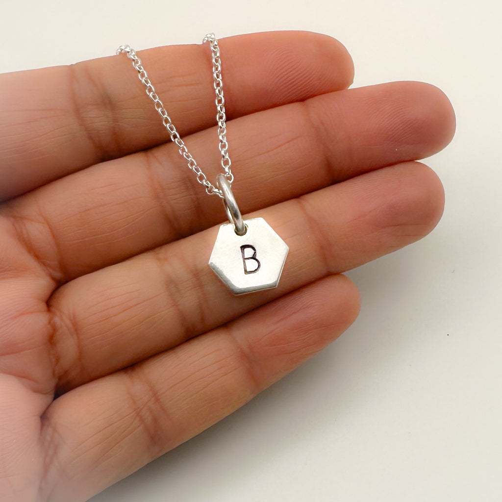 Silver necklace with a hexagonal pendant featuring the letter 'B' held in a hand and handmade in Nottingham in a sustainable way by Bottlebee