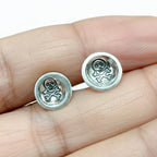 Silver skull and crossbones earrings held between fingers against a white background handmade by a small business called Bottlebee who makes sustainable jewellery in Nottingham
