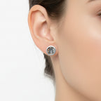 Silver round skull and crossbone earrings worn by a woman with dark hair on a light background handmade by a small business called Bottlebee who makes sustainable jewellery in Nottingham