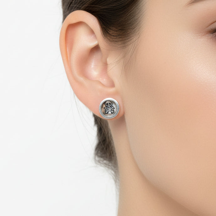 Silver round skull and crossbone earrings worn by a woman with dark hair on a light background handmade by a small business called Bottlebee who makes sustainable jewellery in Nottingham