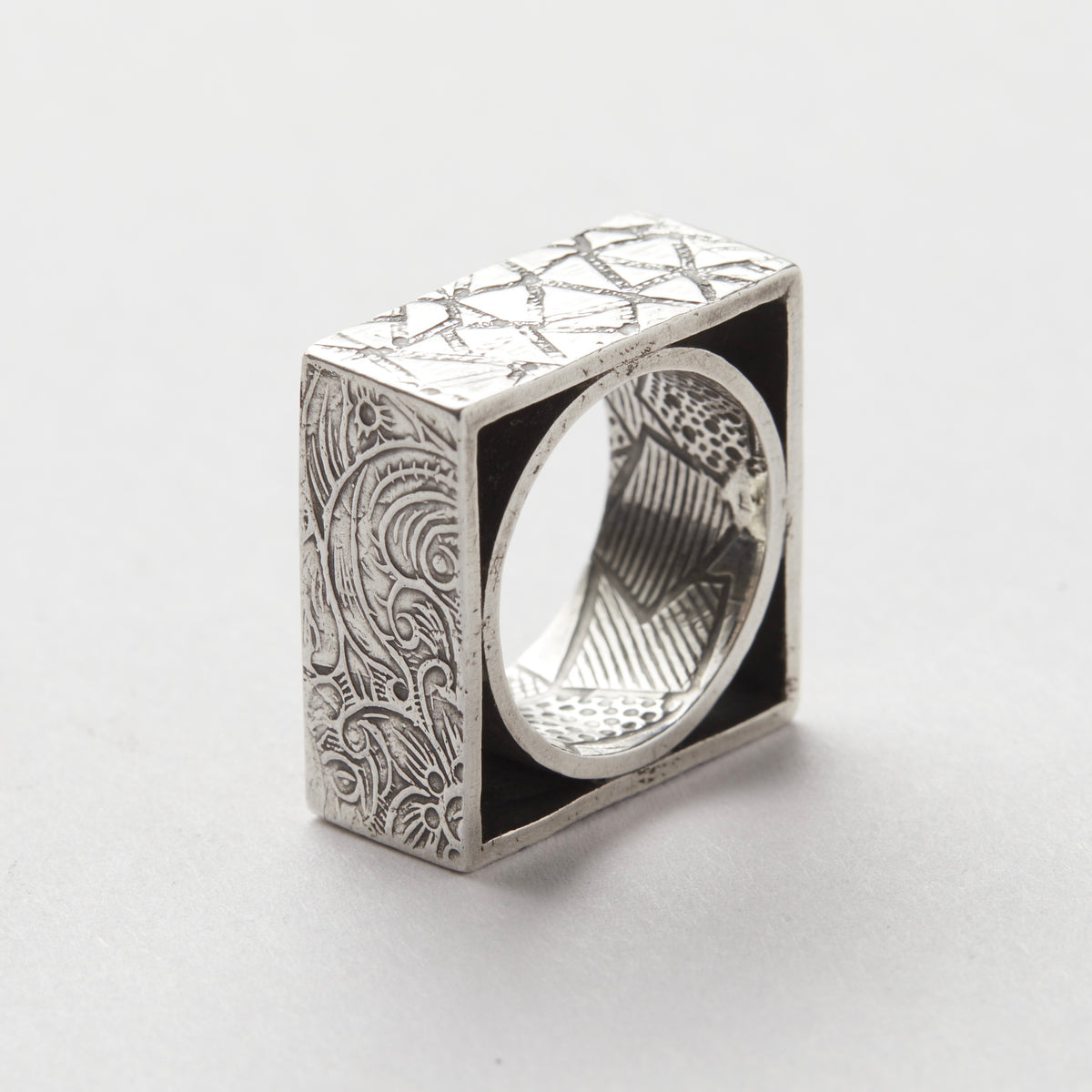 Silver ring with intricate patterns on each side a white background