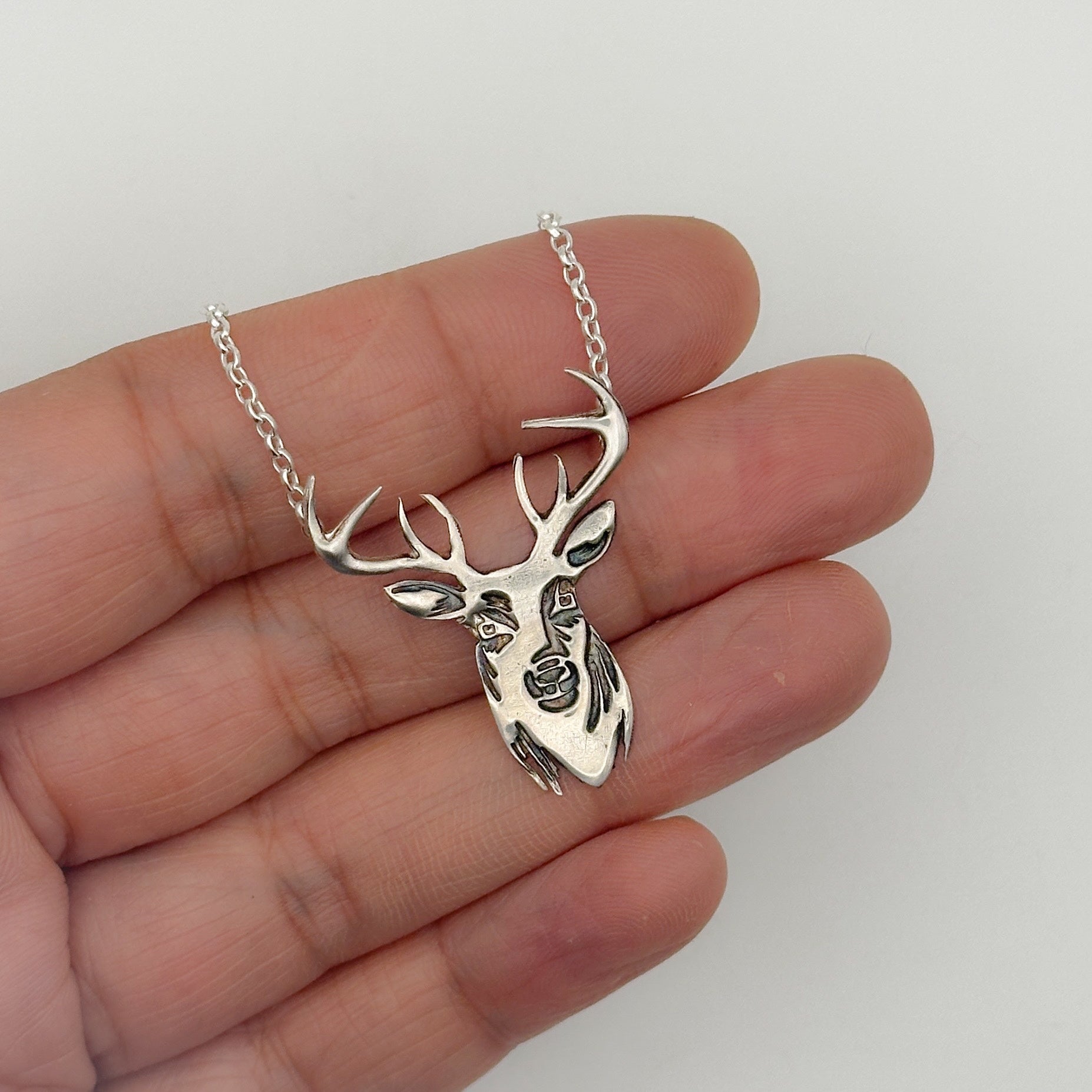 Silver handmade deer head pendant with a belcher chain held in a hand against a white background
