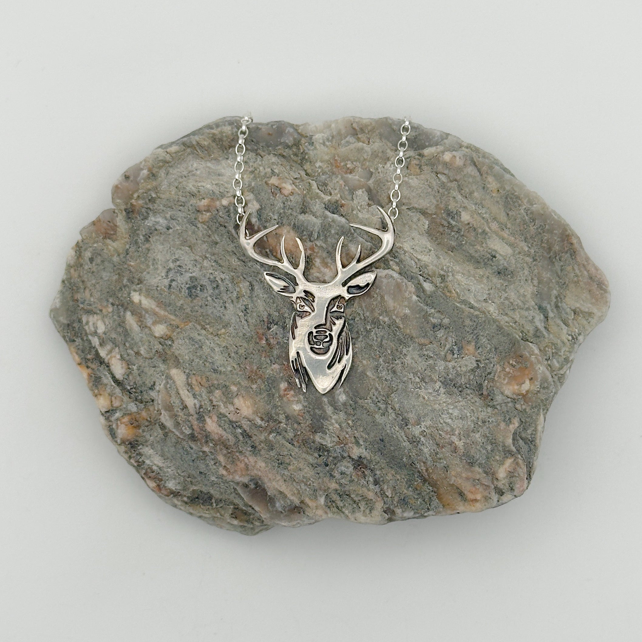 Handmade sterling silver deer head necklace displayed on a rock, made by Bottlebee in Nottingham