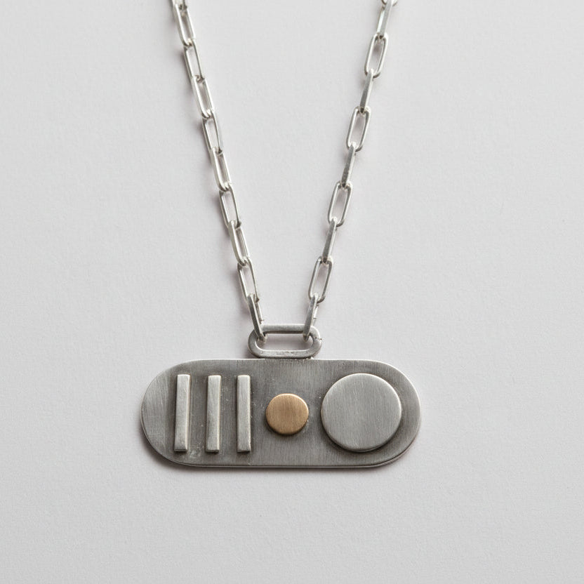 Silver necklace with a unique silver and gold pendant with a silver paperclip chain on a light grey background made by Bottlebee in Nottingham