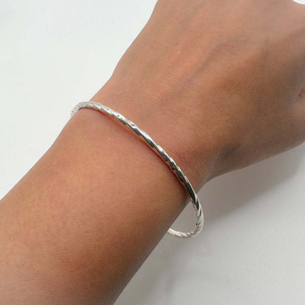 handmade silver bangle on a hand with a light grey background