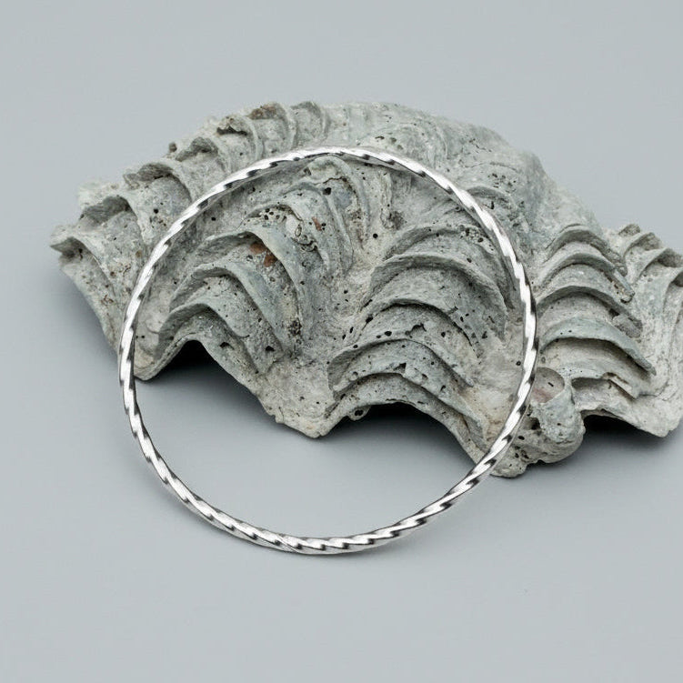 Handmade solid silver bangle on a shell and wooden background