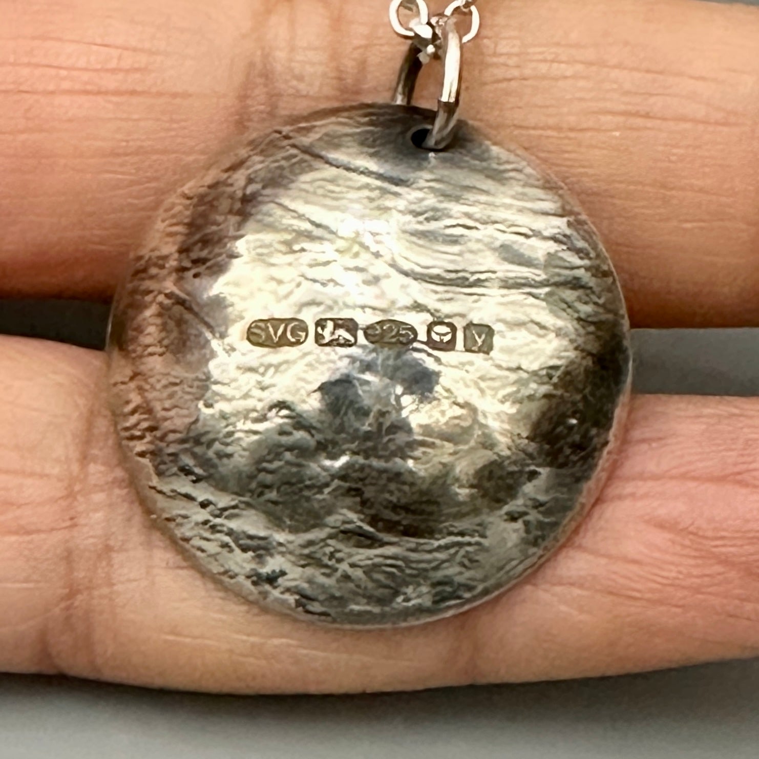 Handmade sterling silver necklace with a hallmark on the back of the pendant held between fingers