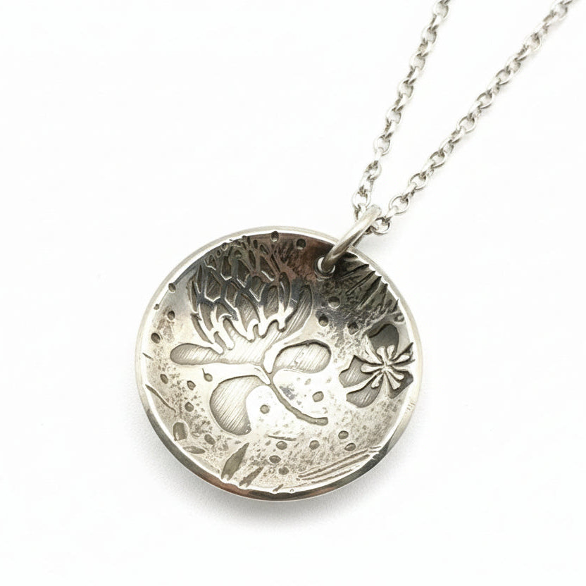 Silver pendant with intricate floral design on a ruler for scale